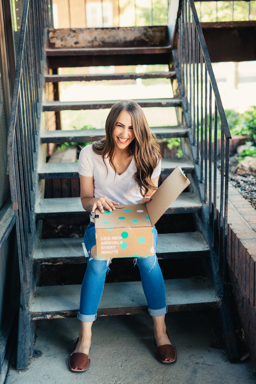 Girl with long brown curled hair in white madewell v-neck unboxing thredup box