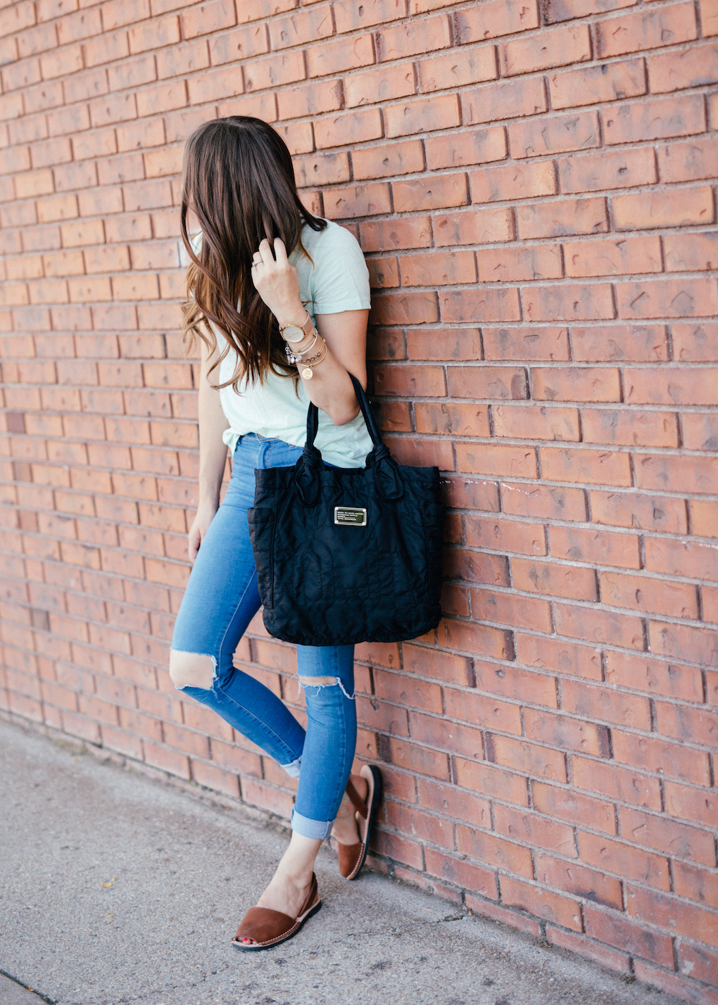 Girl with long brown curled hair wearing distressed skinny jeans, mint madewell tee, marc jacobs bag, and PONS shoes
