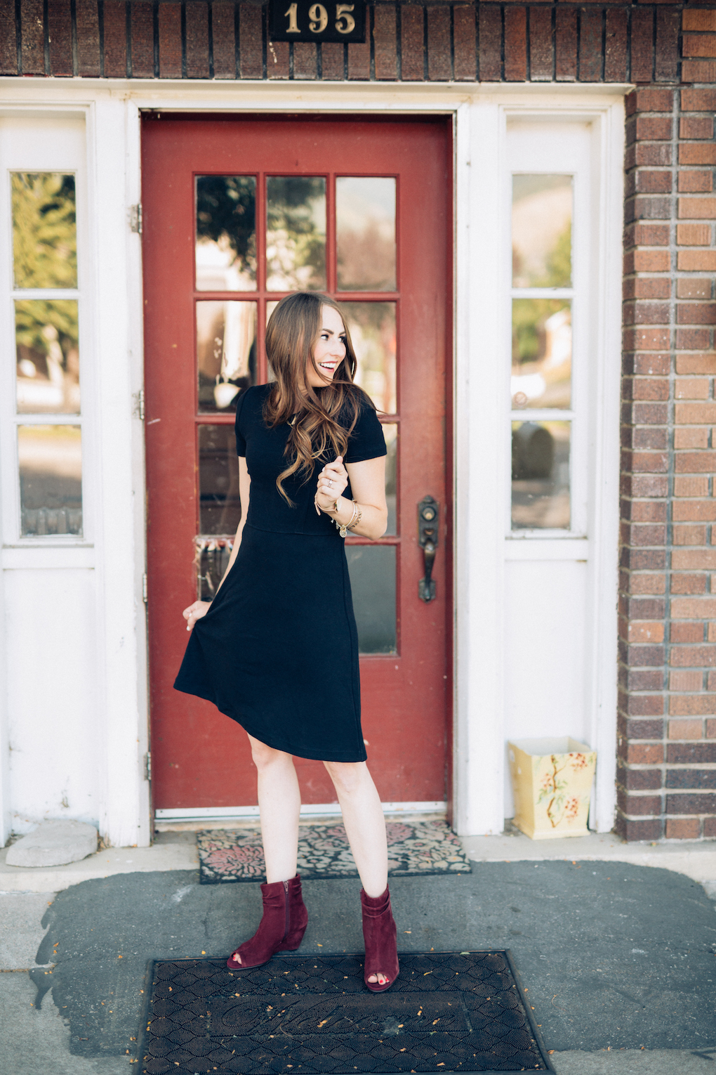 Girl with long brown hair wearing black madewell dress and maroon wedges looking over her shoulder