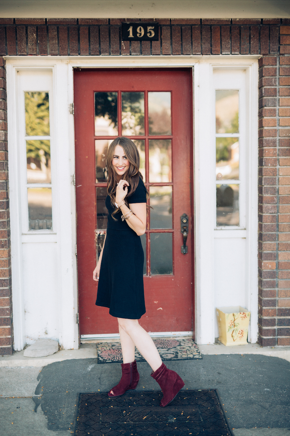 Girl with long brown hair wearing black madewell dress and maroon wedges 