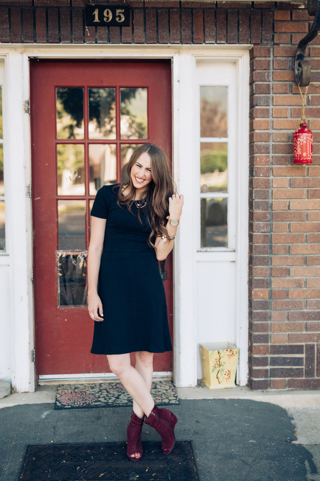 Girl with long brown hair wearing black madewell dress and maroon wedges laughing