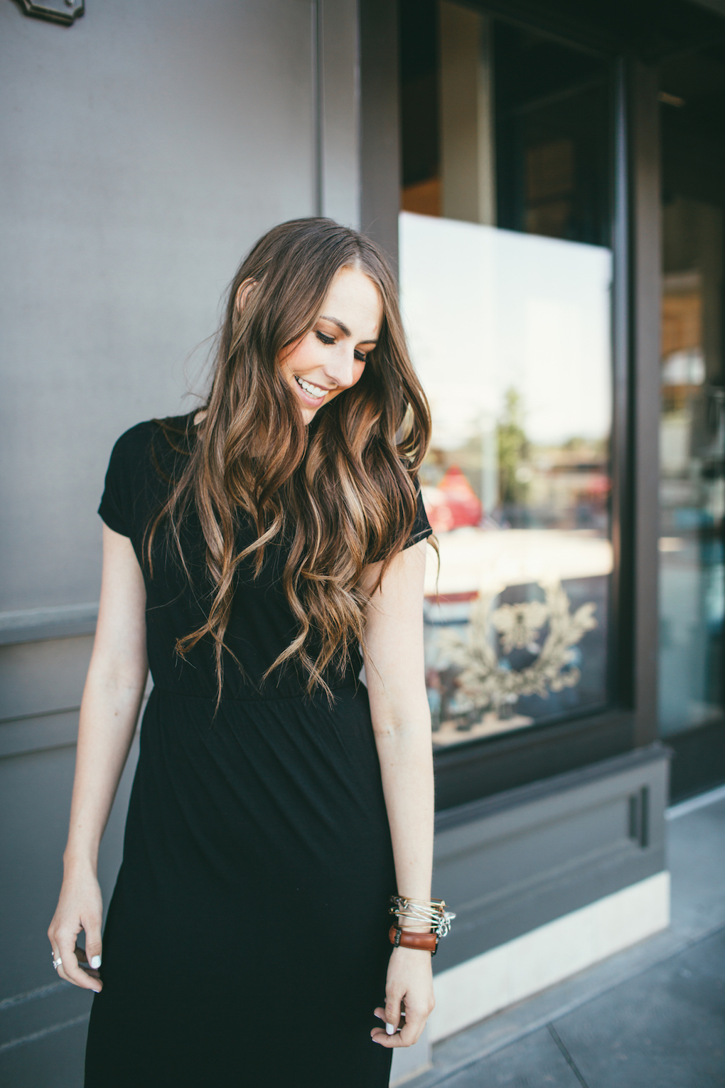 girl wearing black dress with rouched waist with long brown loosely curled hair looking down with eyes closed