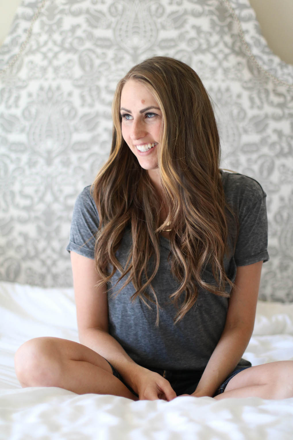 girl sitting on bed in grey tee with brown hair
