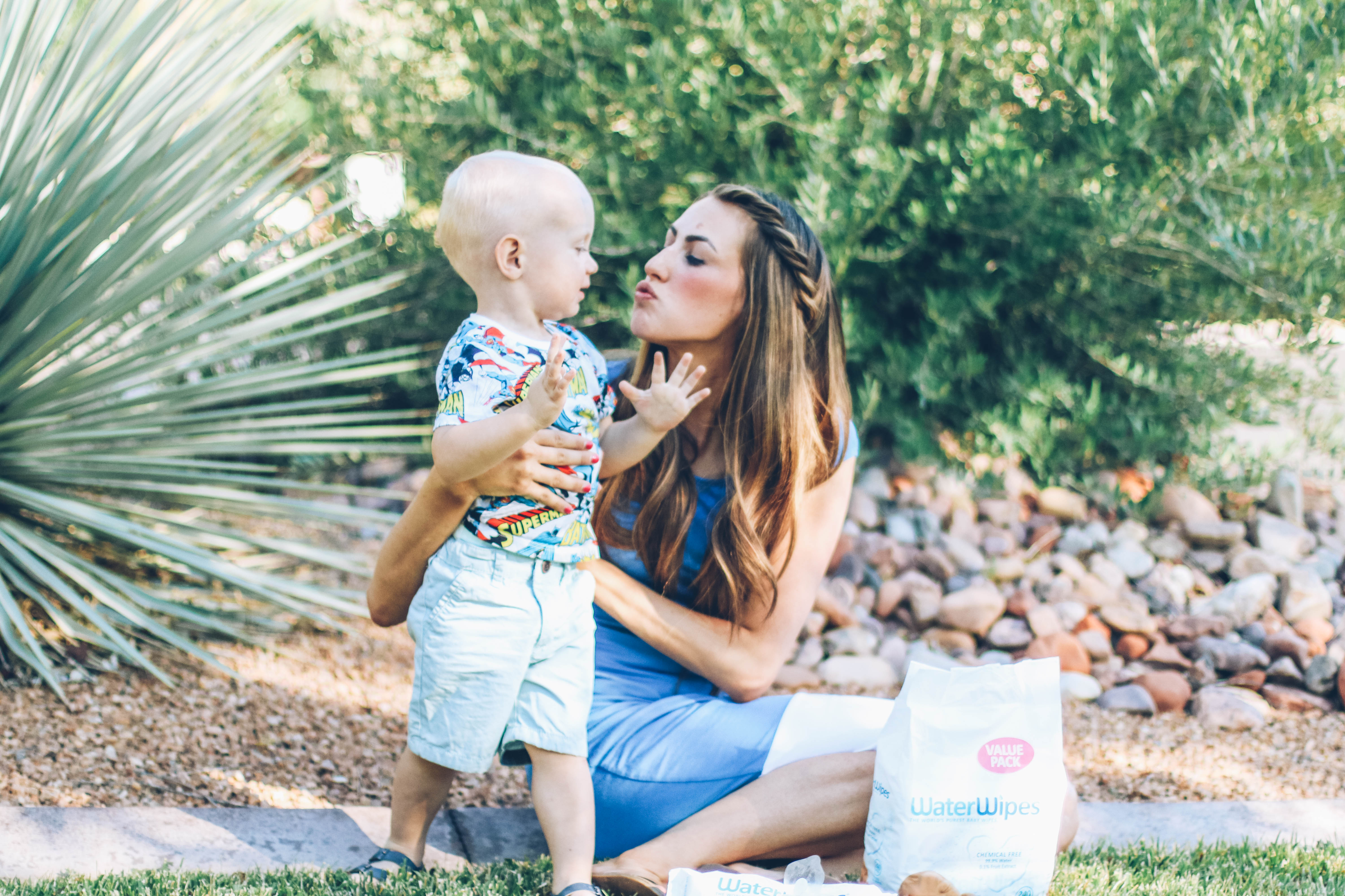 Mom and baby kissing on grass baby wearing a super hero tee with water wipes