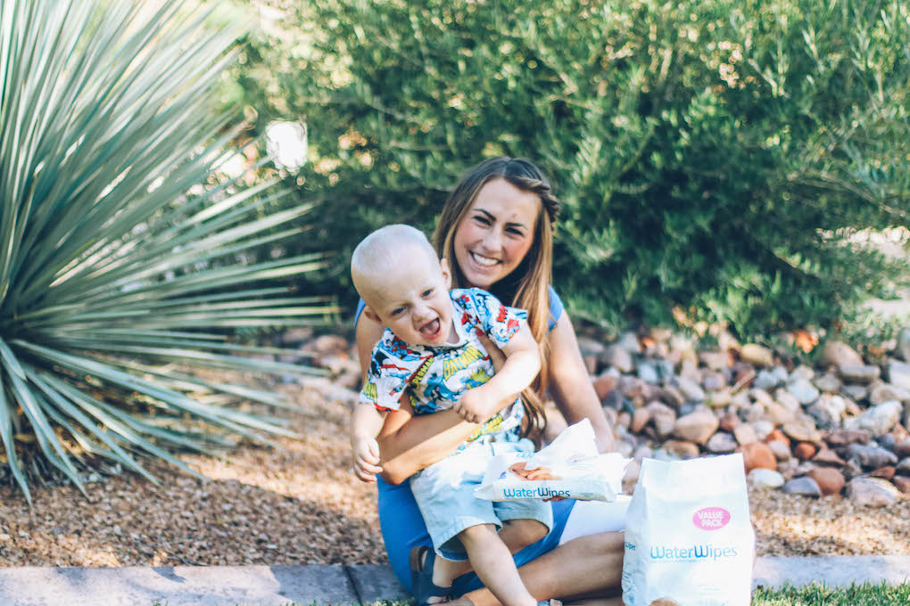 Mom and baby giggling on grass baby wearing a super hero tee with water wipes