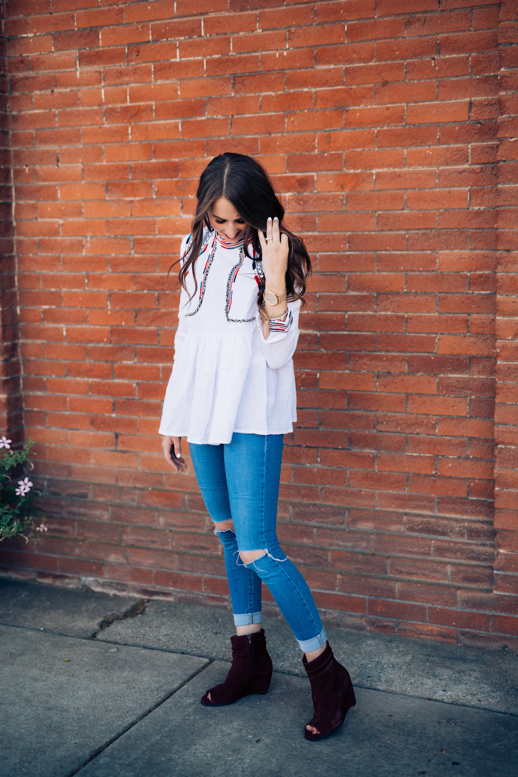 Girl in white peplum top with bright colored embroidery and skinny jeans with maroon booties 