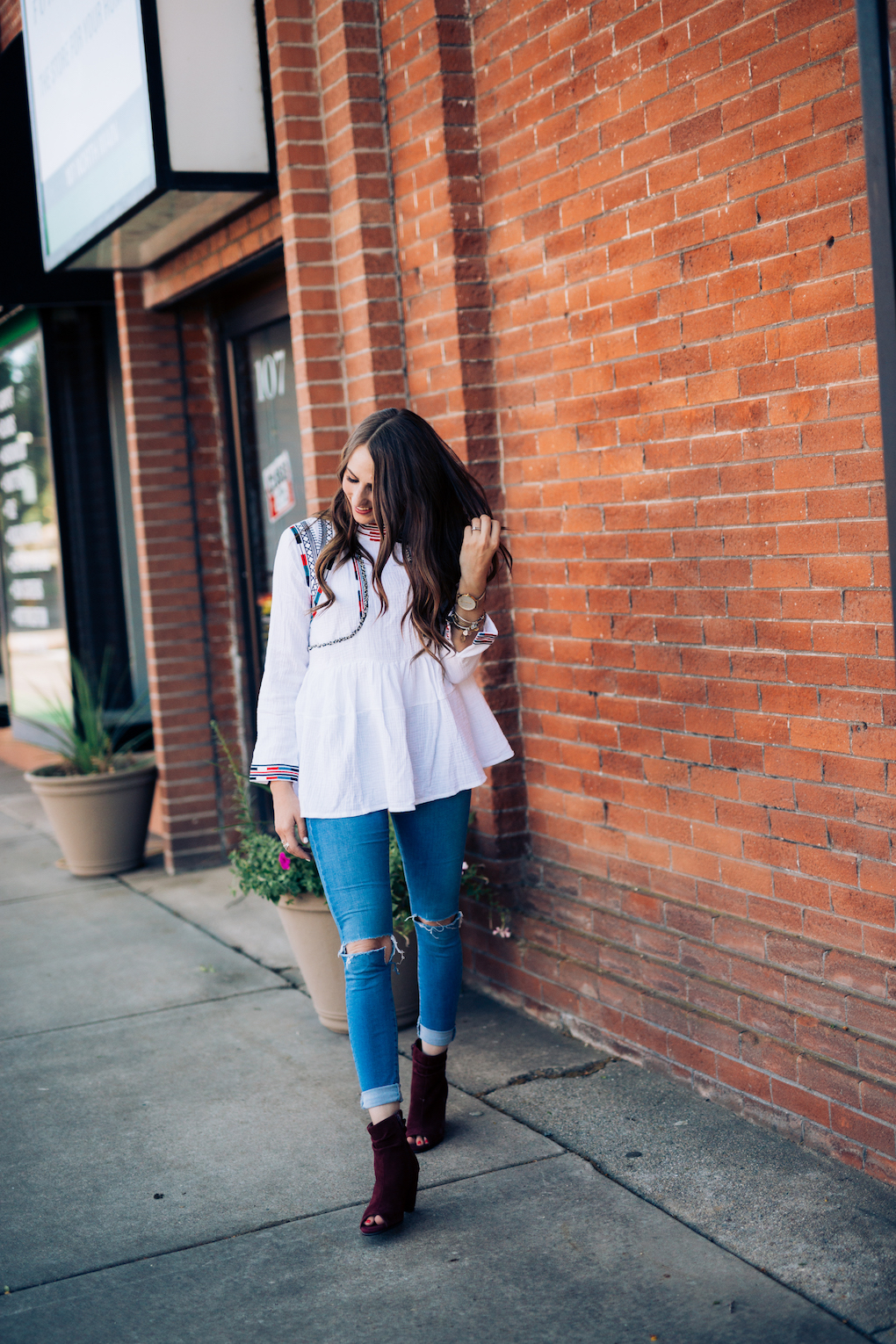 Girl in white peplum top with bright colored embroidery and skinny jeans with maroon booties