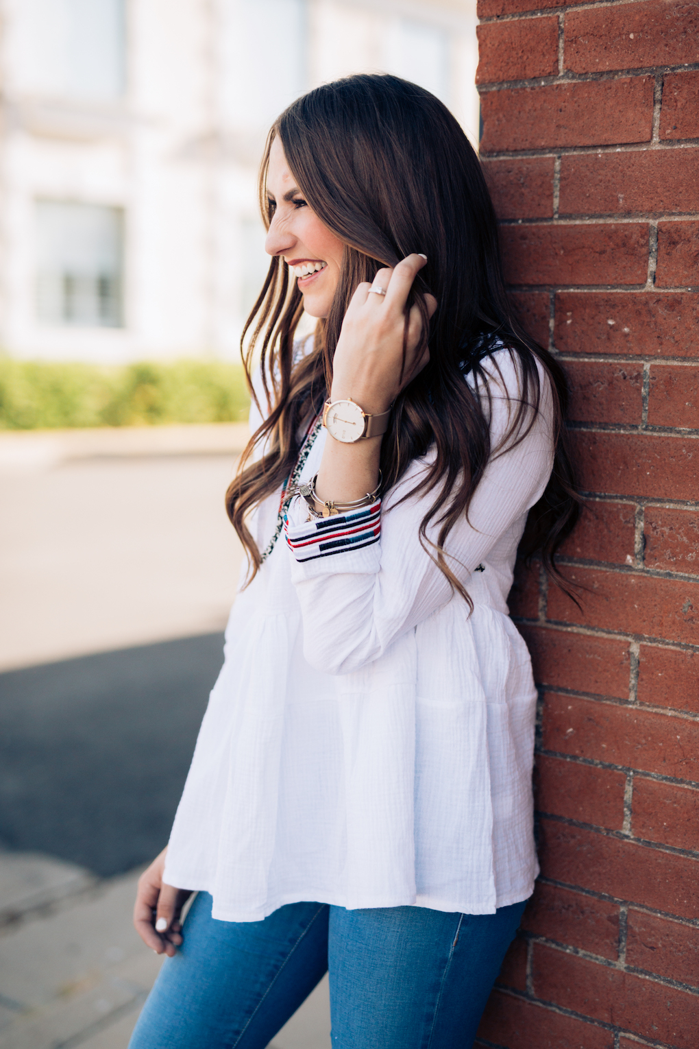 Girl in white peplum top with bright colored embroidery and skinny jeans with maroon booties and arvo watch with alex and ani bracelets