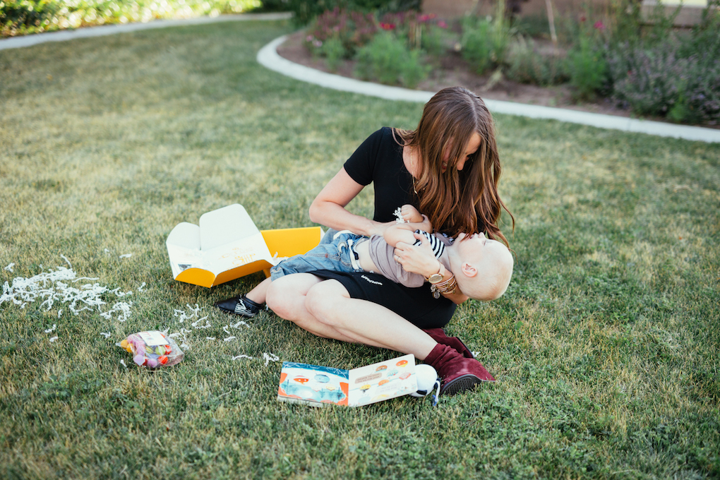 Mom and little boy opening up book subscription box on the grass