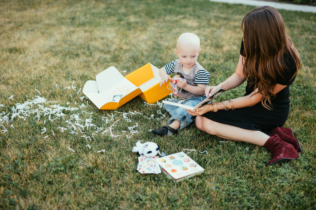 Mom and little boy opening up book subscription box on the grass