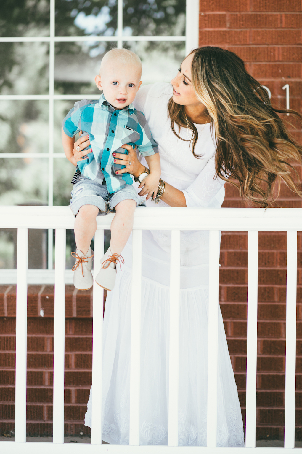 Mom and little boy sitting on porch steps mom wearing white embroidered maxi dress with long loose caramel curls little boy in blue and turquoise plaid shirt and cut off shorts