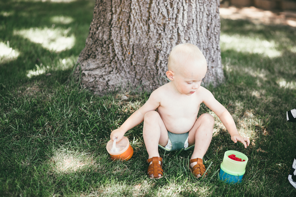 Little boy sitting by tree in short swimmers holding treat container