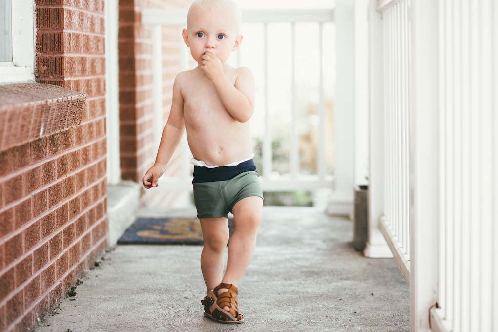 Little boy standing on porch with green short swimmers on