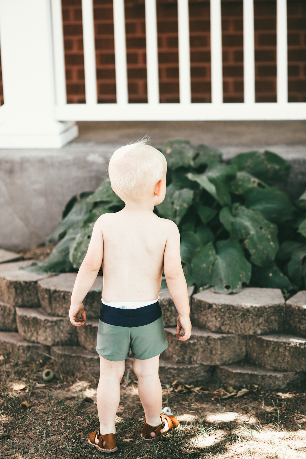 Little boy wearing short green swimmers standing backwards