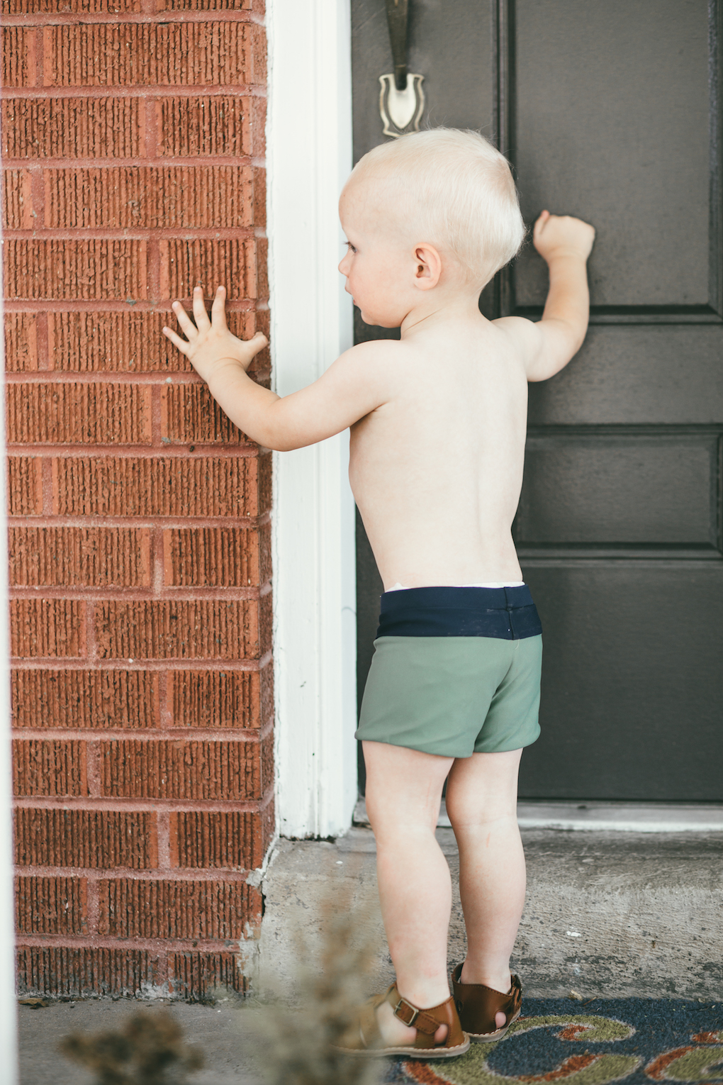 little boy wearing green swimmers knocking on the door
