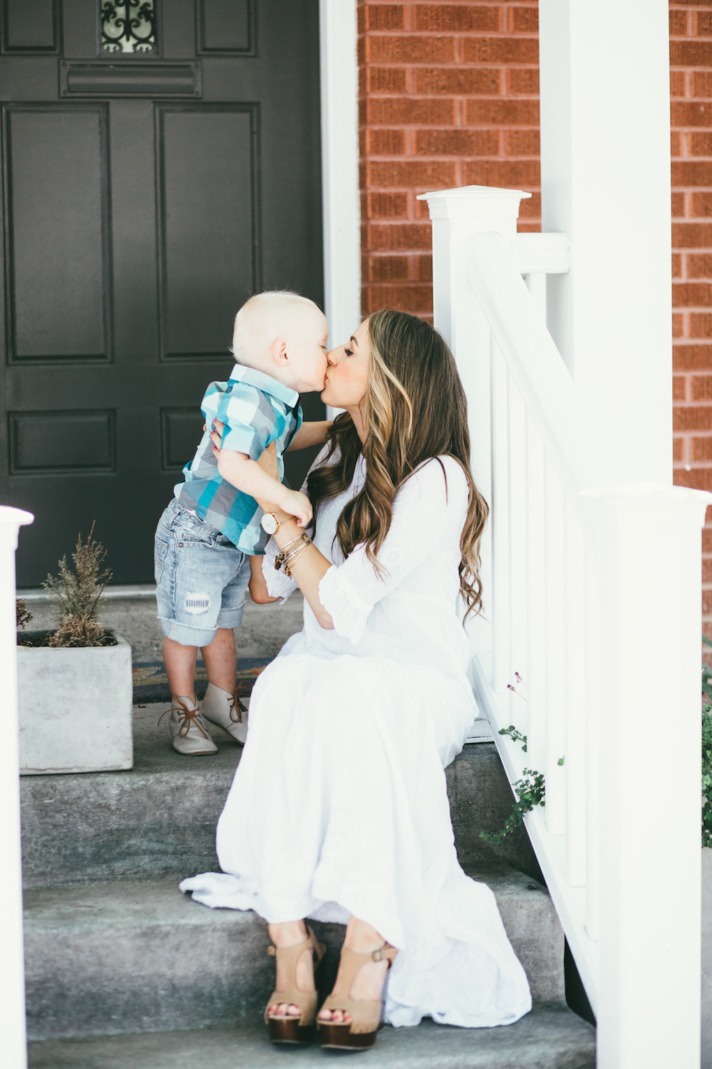 Mom and little boy sitting on porch steps mom wearing white embroidered maxi dress with long loose caramel curls little boy in blue and turquoise plaid shirt and cut off shorts
