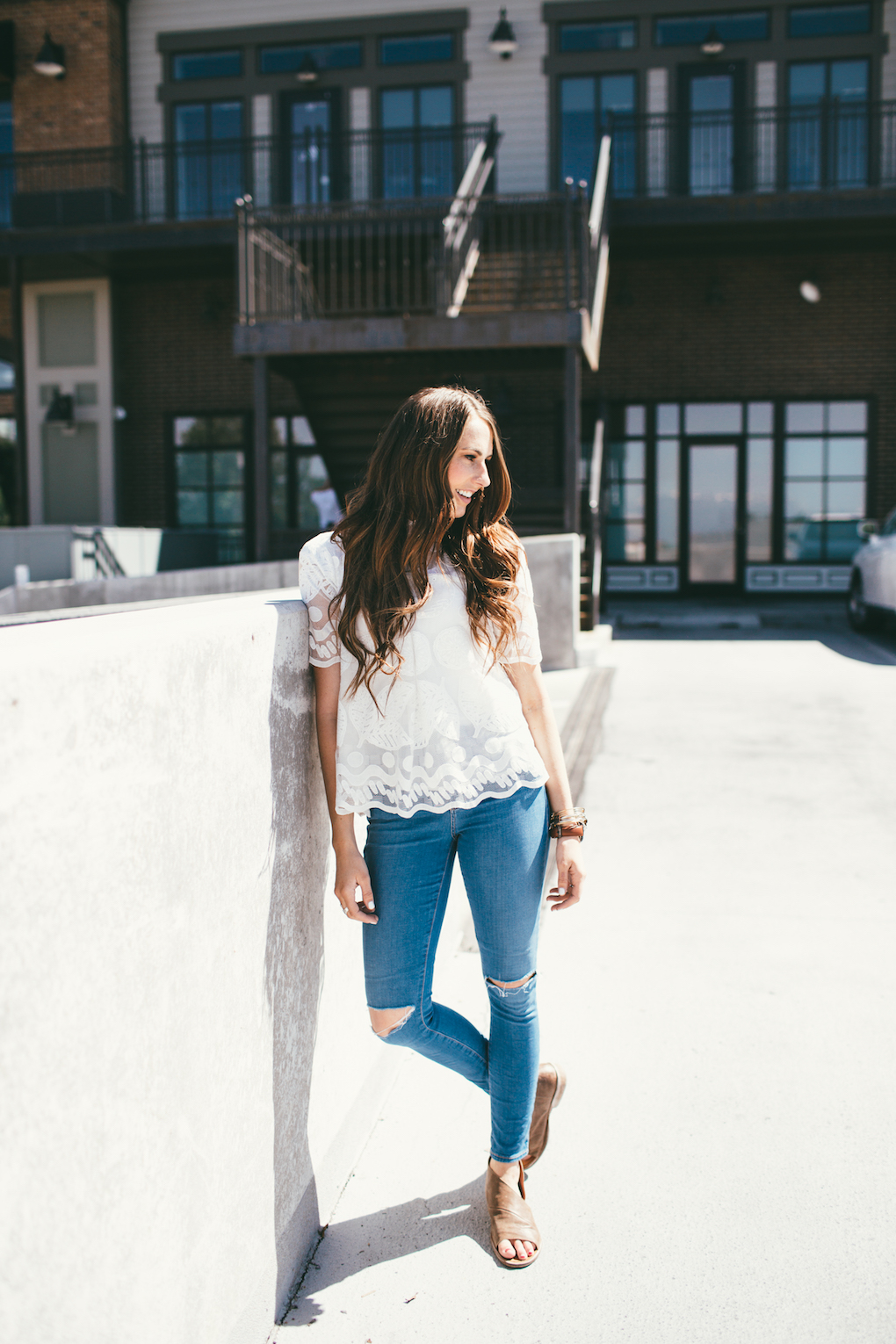 Girl standing in distressed denim jeans free people brown sandals and anthropologie white lemon lace top with long brown hair loosely curled
