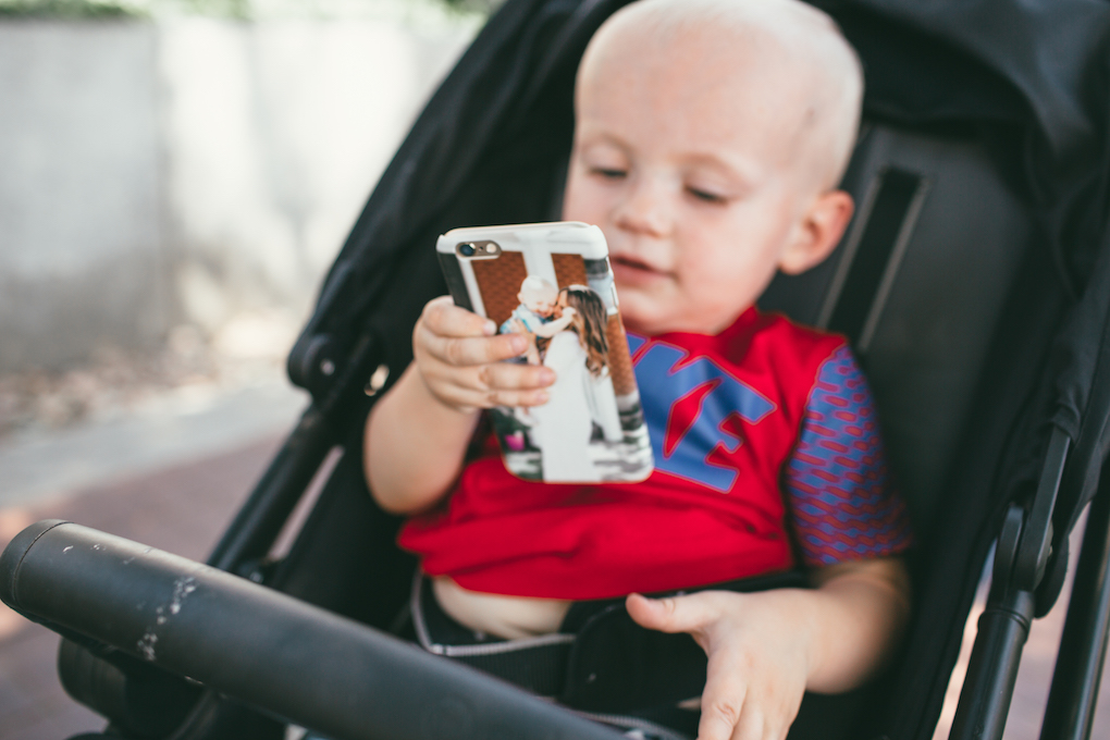 Little boy in red Nike shirt sitting in stroller holding phone in personalized phone case