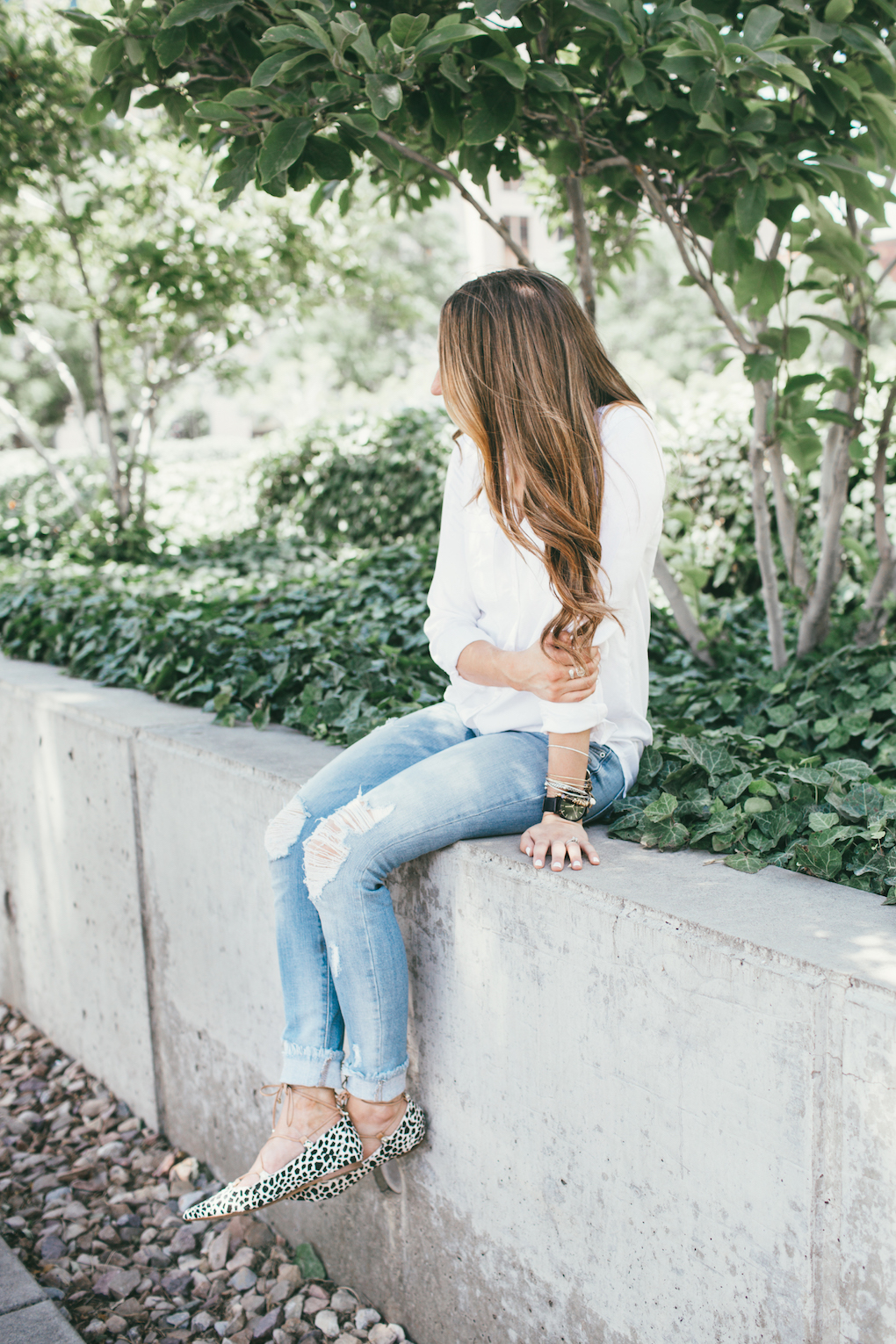 Girl wearing white button up with long loose brown curls and skinny distressed denim