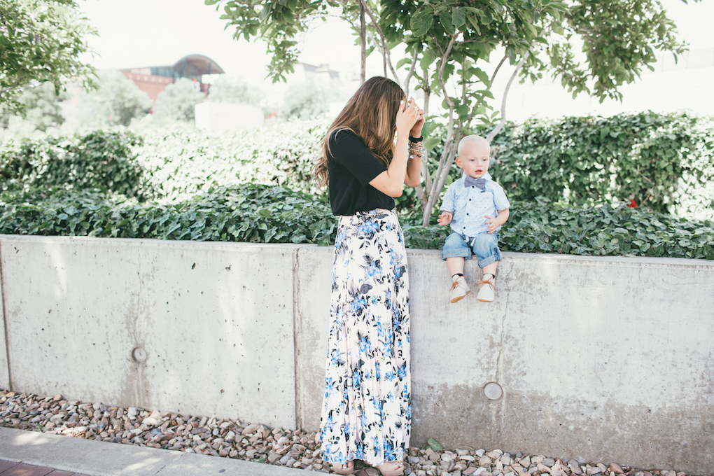 Mom and little boy in dress clothes or sunday best standing outside mom in floral pleated skirt with black top little boy in painter pants and hurley button up with baby bow tie