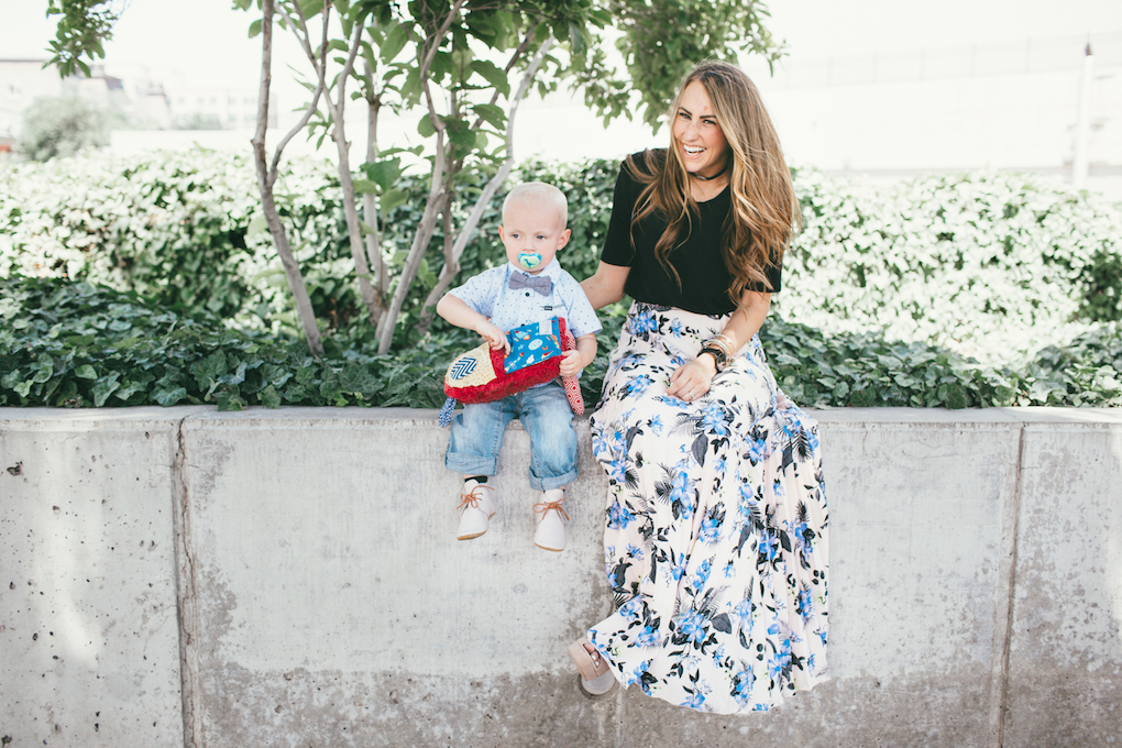 Mom and little boy in dress clothes or sunday best standing outside mom in floral pleated skirt with black top little boy in painter pants and hurley button up with baby bow tie