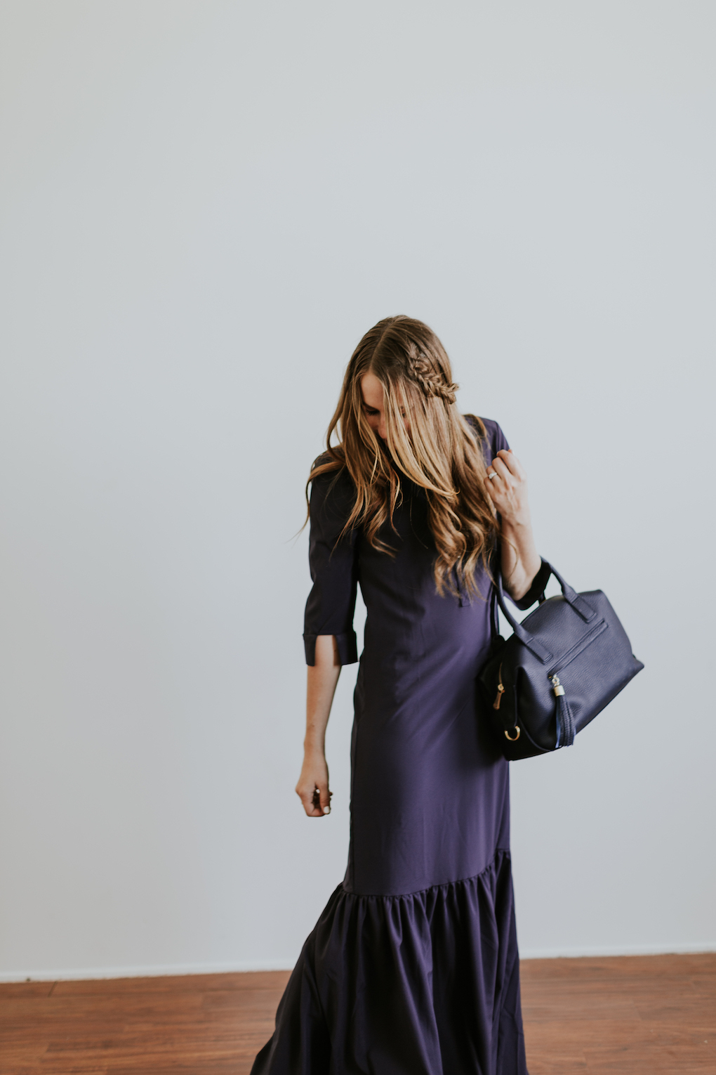 Girl with fishtail braid wearing long navy maxi dress with ruffle and a navy gigi new york bag