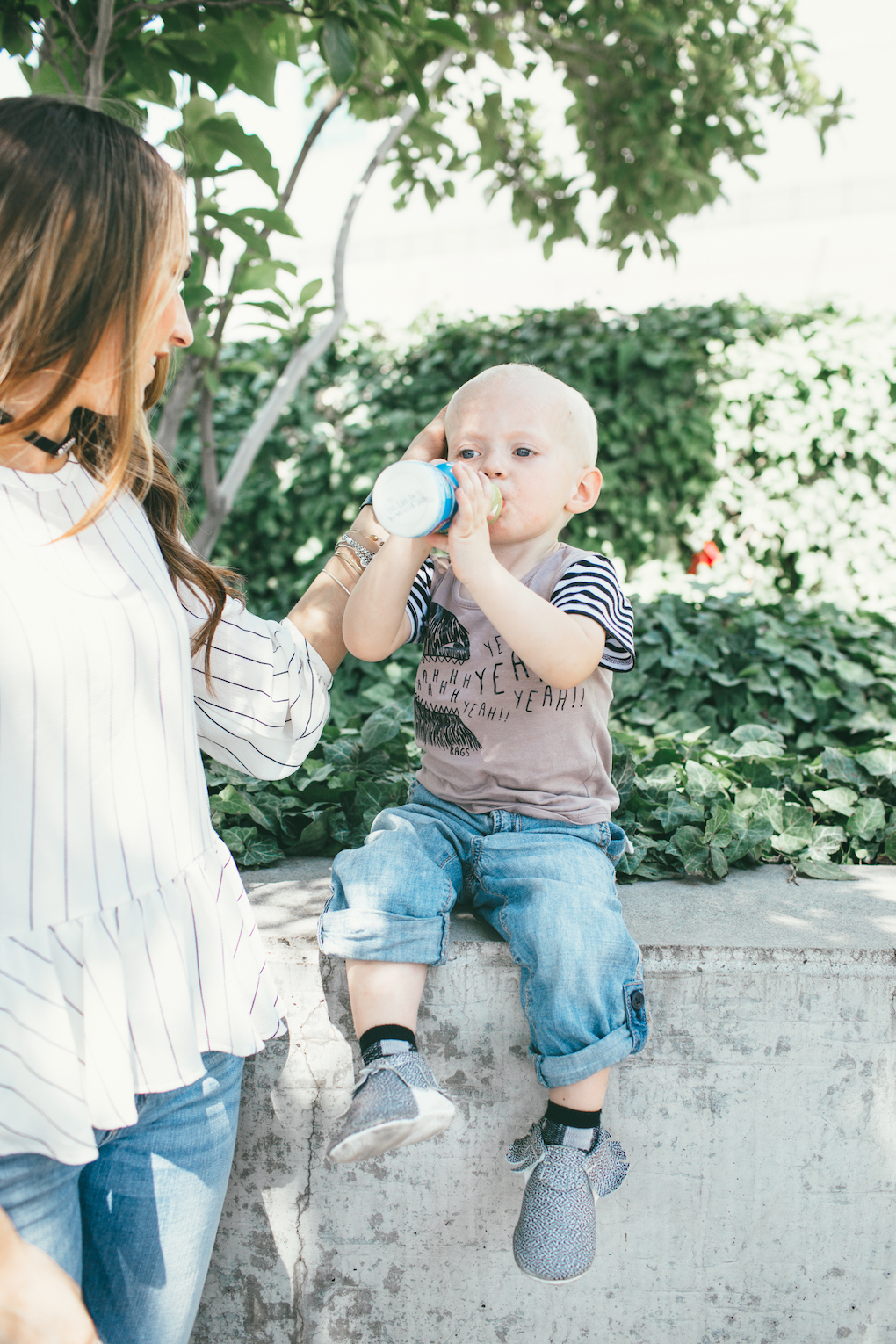Mom in white stripe peplum black choker and distressed denim rubbing little boys head little boy wearing rags to raches tee shirt with rolled up denim and freshly picked moccs