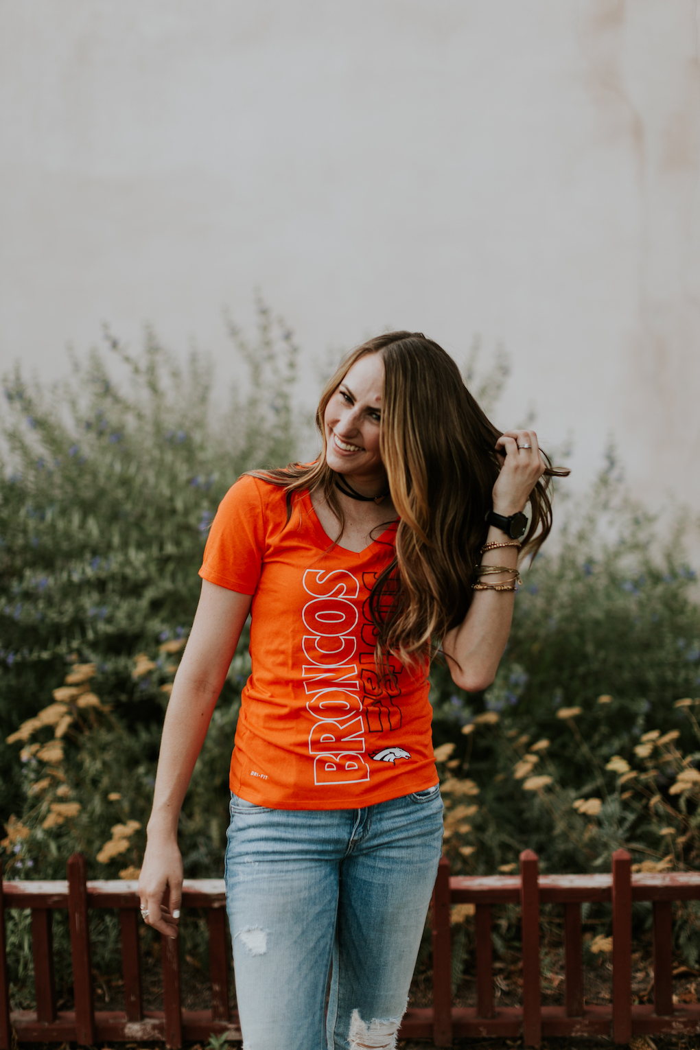Womens NFL Broncos T-Shirt girl wearing bright orange Broncos Tee shirt with brown curled hair and skinny distressed denim