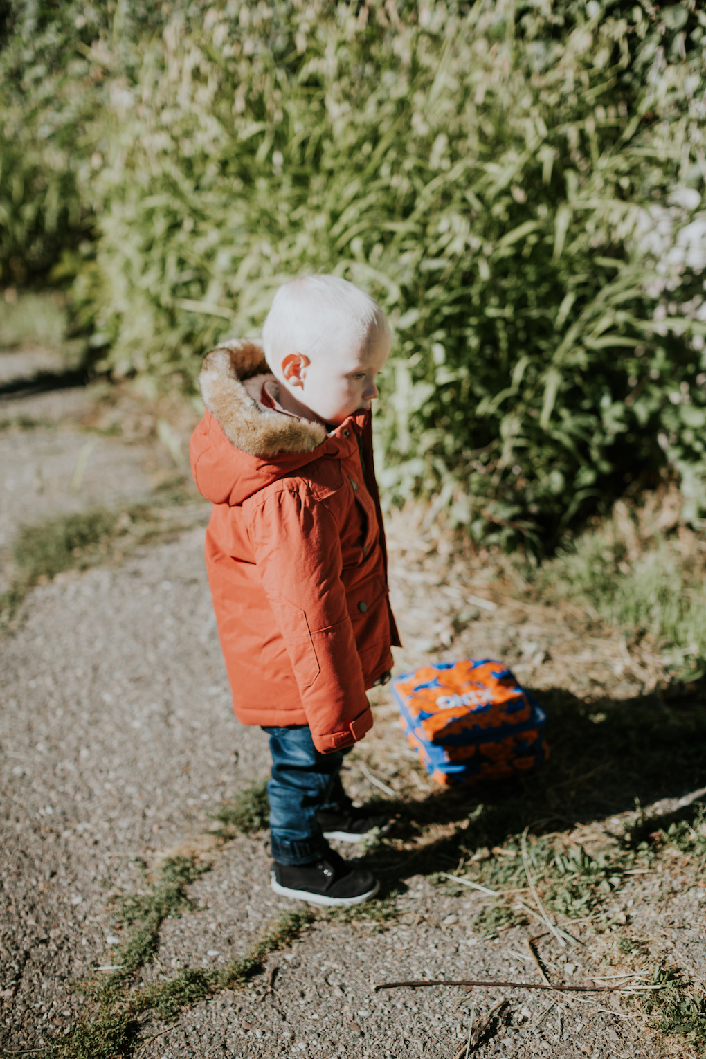 little boy running in orange coat with fur on the hood and denim joggers with black toms