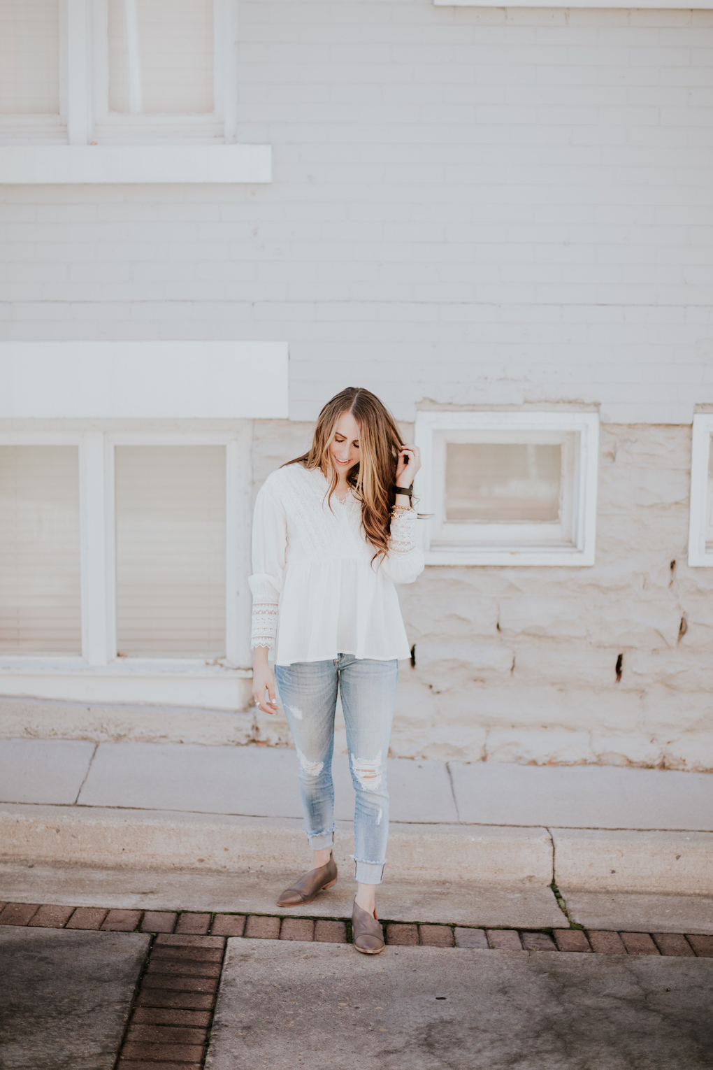 Girl wearing white textured top with distressed light denim skinny jeans and free people booties