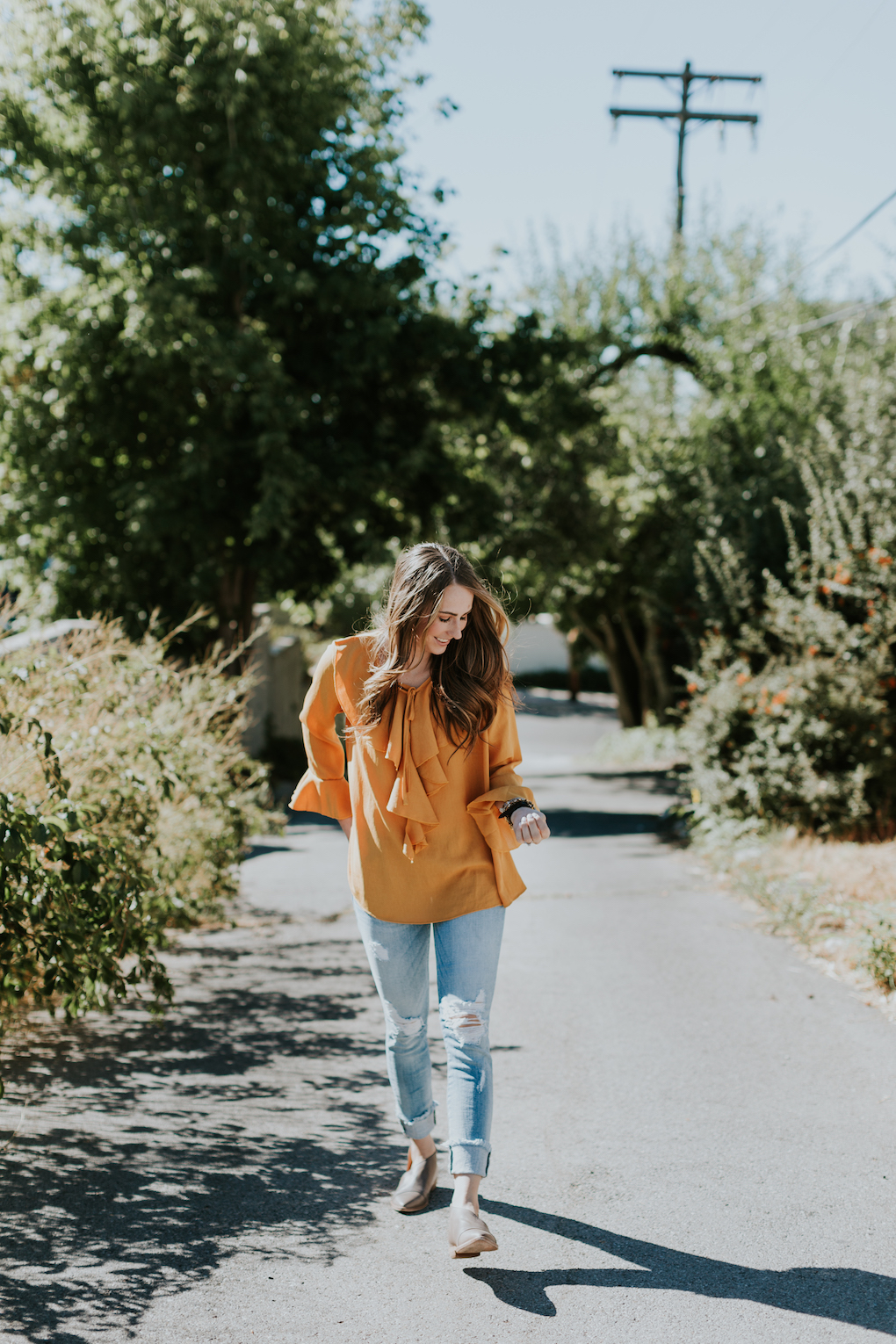 girl with brown caramel hair wearing mustard orange sheer ruffle top with distressed jeans