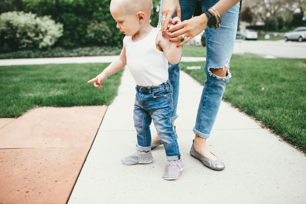 mom and toddler boy walking down sidewalk little boy in white wife beater tank top and distressed jeans with freshly picked moccs