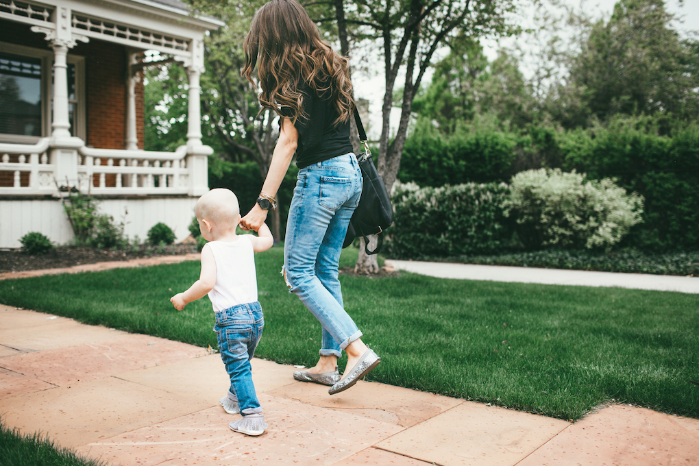 mom and toddler boy walking down sidewalk little boy in white wife beater tank top and distressed jeans with freshly picked moccs mom in distressed denim with black free people top yosi samra flats and black fawn design bag 