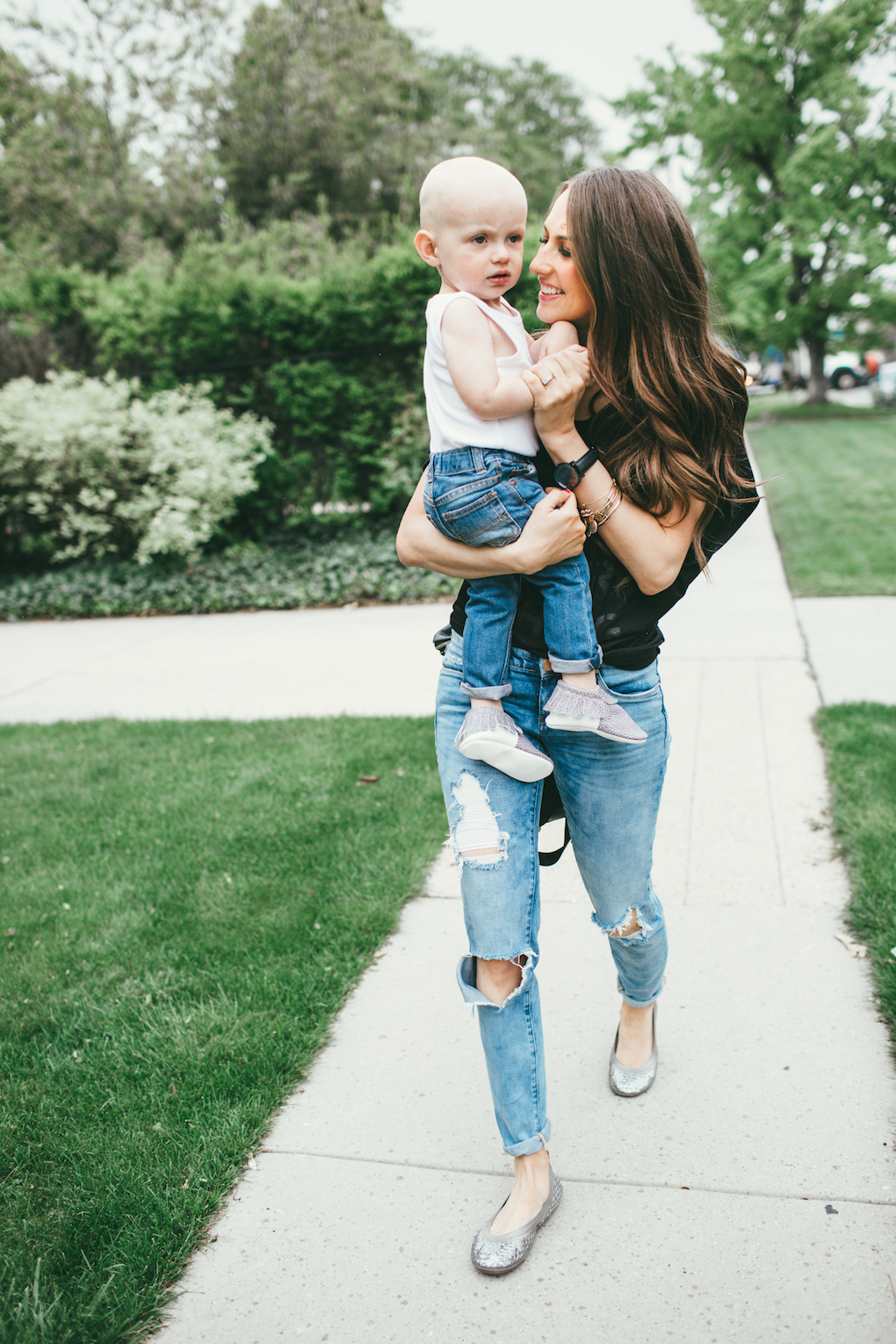 mom and toddler boy walking down sidewalk little boy in white wife beater tank top and distressed jeans with freshly picked moccs mom in distressed denim with black free people top yosi samra flats and black fawn design bag 