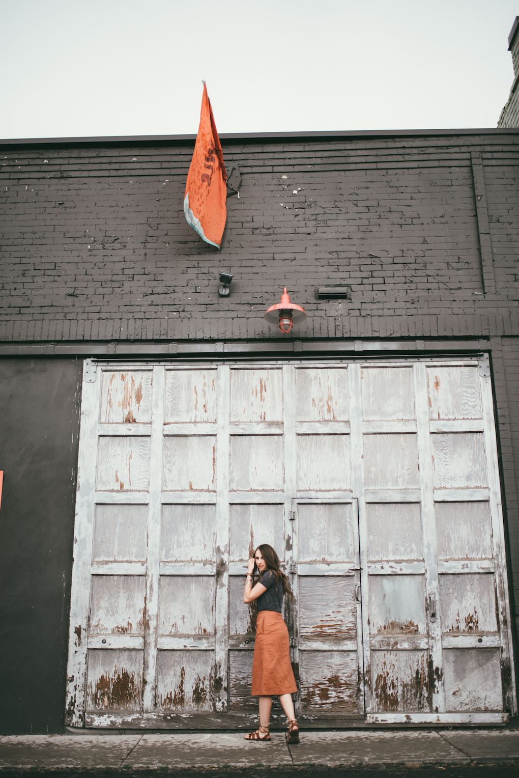 orange button up midi skirt with grey tee shirt girl standing in front of old distressed white garage door