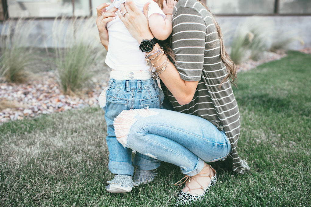 mom and little boy playing on the grass mom in distressed denim green stripe shirt and leopard flats looking at little boy laughing little boy in skinny jeans moccasins and a graphic tee