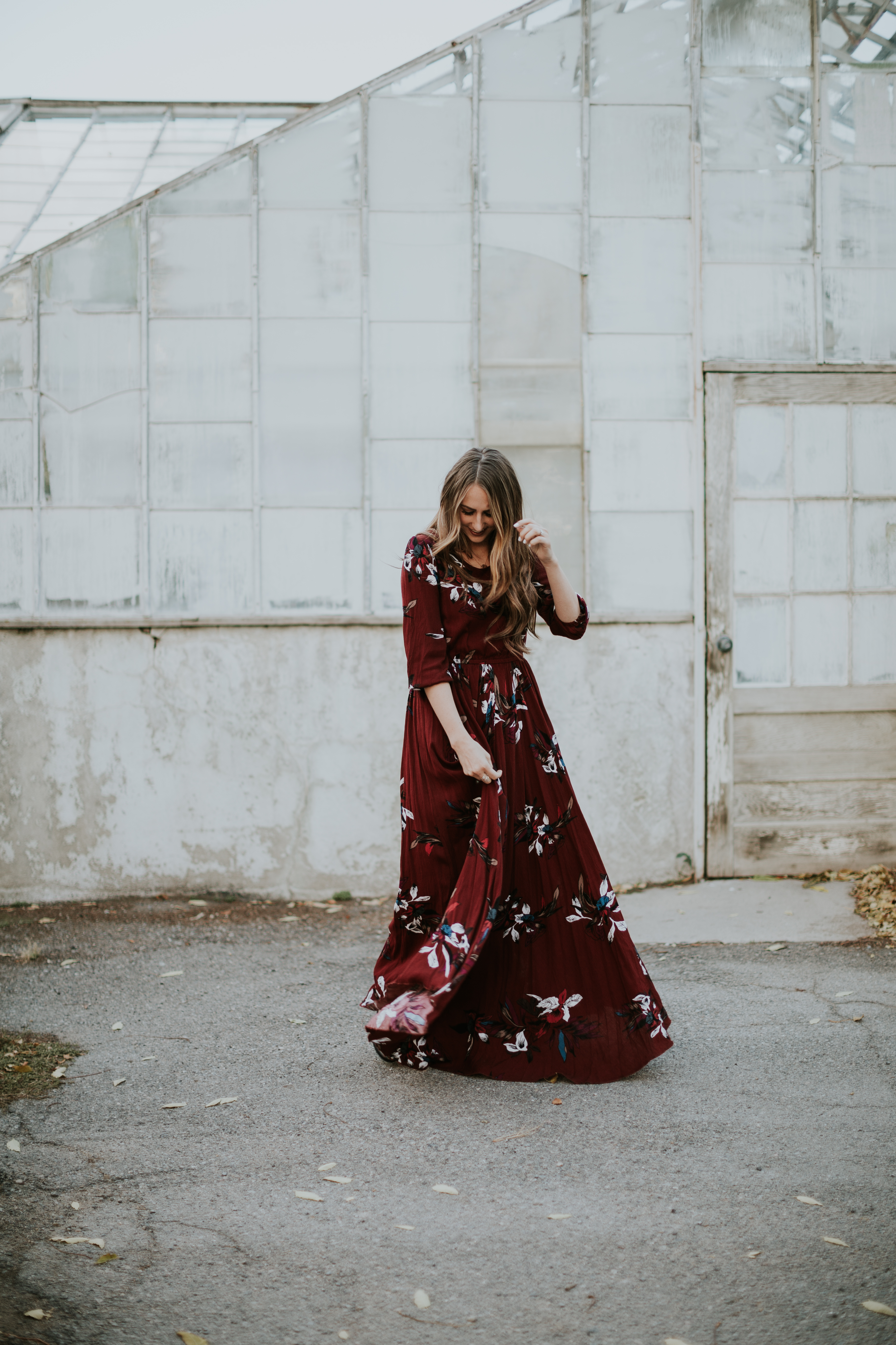 floral maroon maxi dress with girl standing in front of a green house with long brown loosely curled hair with caramel highlights