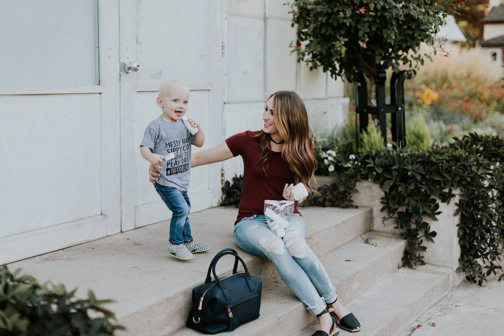 mom and little boy sitting on the stairs with baby pibu products little boy in graphic tee and jeans mom in distressed denim a maroon top and a navy handbag