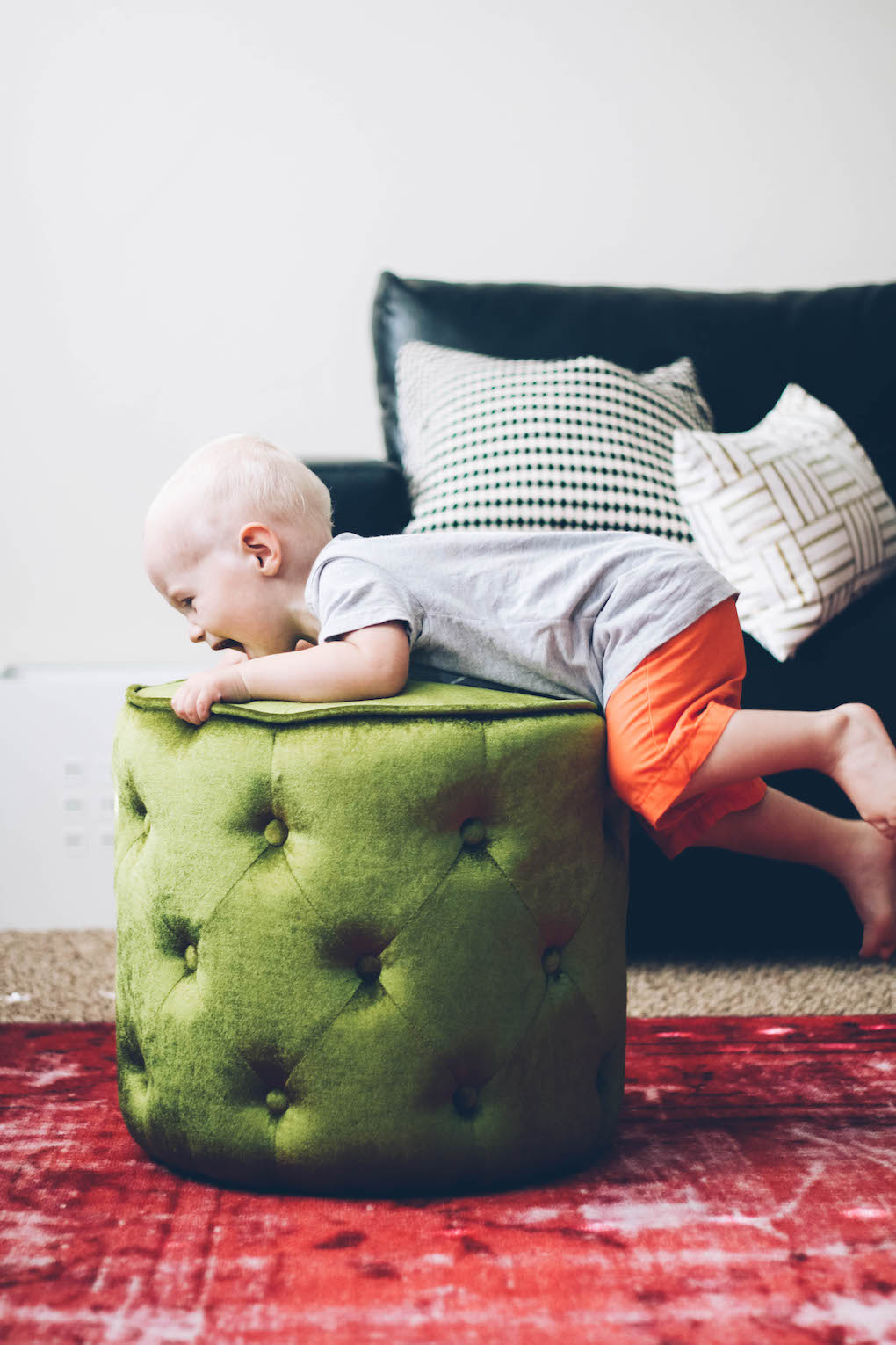 little boy climbing on green ottoman in living room with pink rug