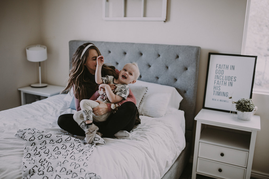 girl sitting on bed giggling in pink top with latterday home print and owl be sweatin headband lisa leonard ring and arvo watch with little boy in rags to raches and freshly picked moccasins