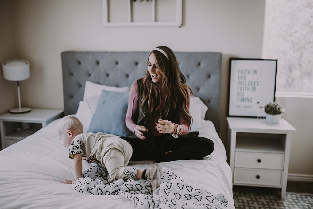 girl sitting on bed giggling in pink top with latterday home print and owl be sweatin headband lisa leonard ring and arvo watch with little boy in rags to raches and freshly picked moccasins