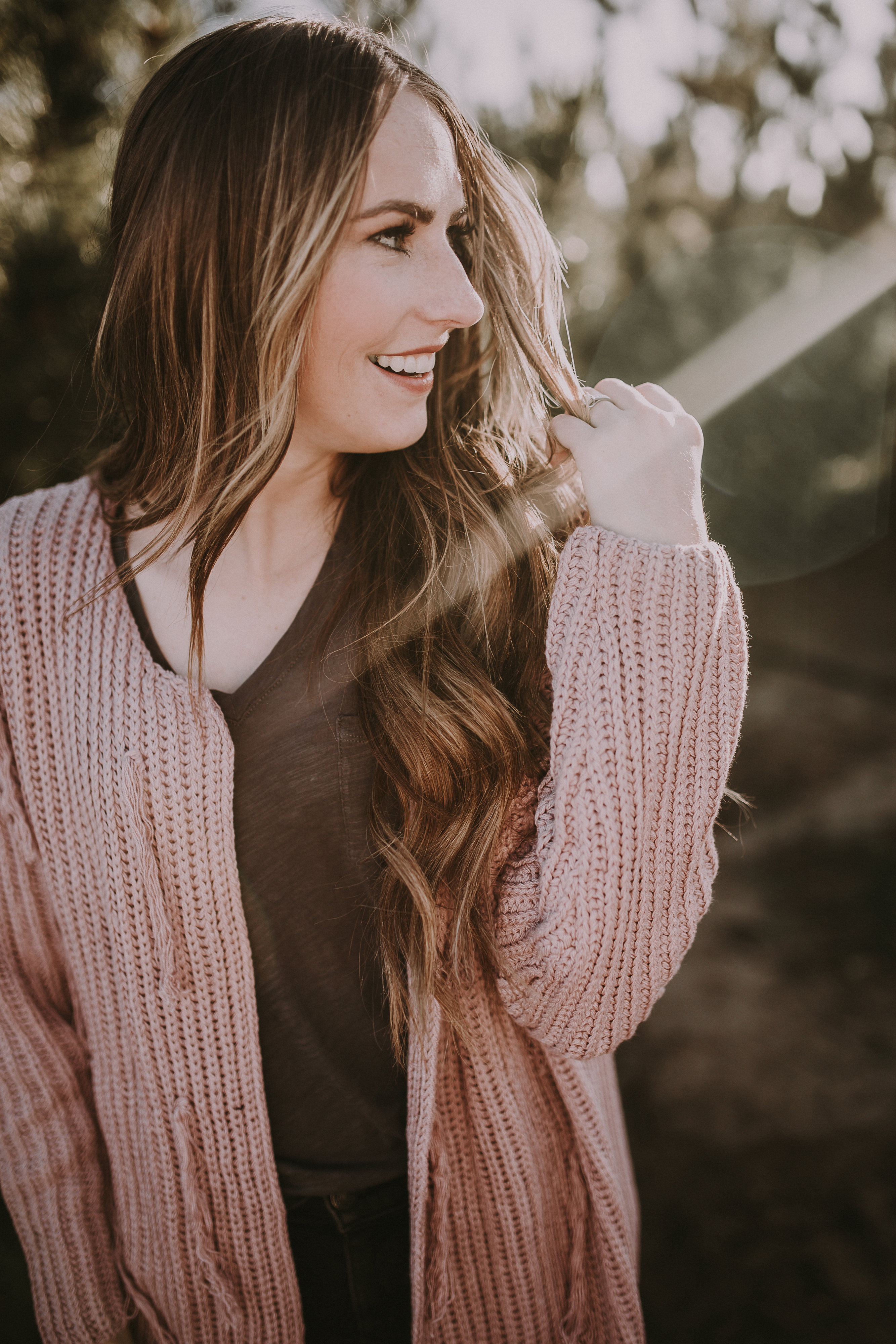 girl in light pink long thick cardigan with grey tee shirt floral booties and black distressed jeans with long loose curled brown and caramel long hair