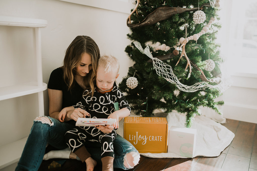 mom and little boy sitting under christmas tree reading book with shape mags, lit joy crate box, and owlet baby monitor