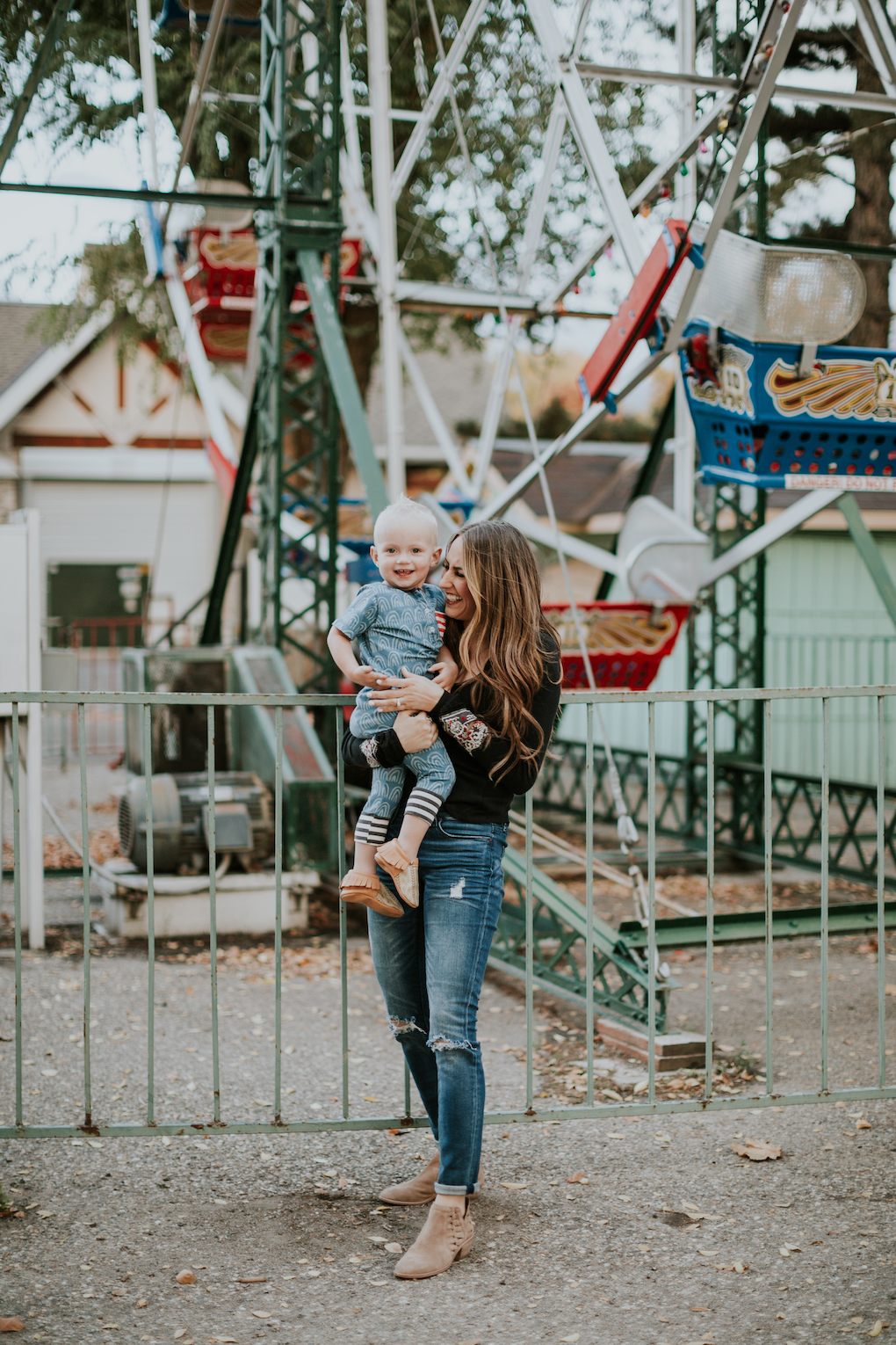 mom and little boy playing at amusement park little boy in rags to raches romper and freshly picked moccasins mom in free people thermal top skinny jeans and brown booties