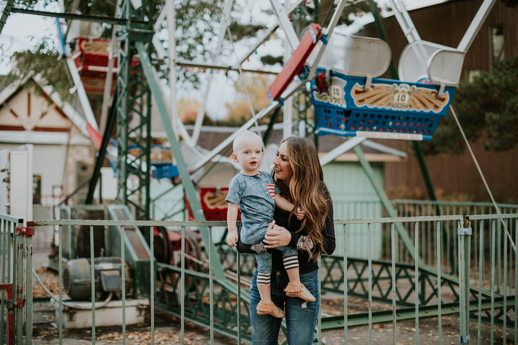 mom and little boy playing at amusement park little boy in rags to raches romper and freshly picked moccasins mom in free people thermal top skinny jeans and brown booties