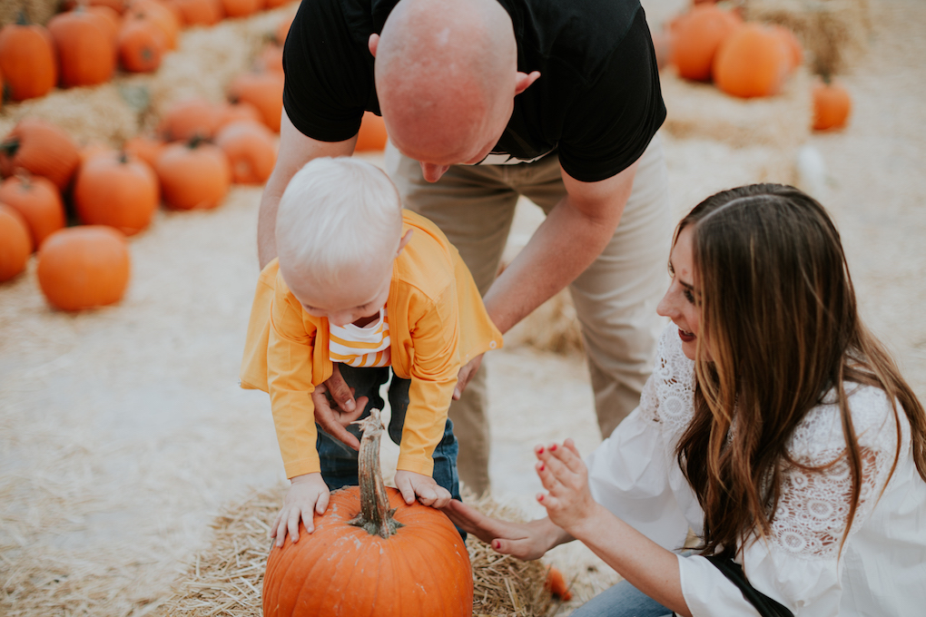 family playing at pumpkin patch mom in white lace top with skinny jeans dad in khaki pants and black tee little boy in june and january newlie diaper bag