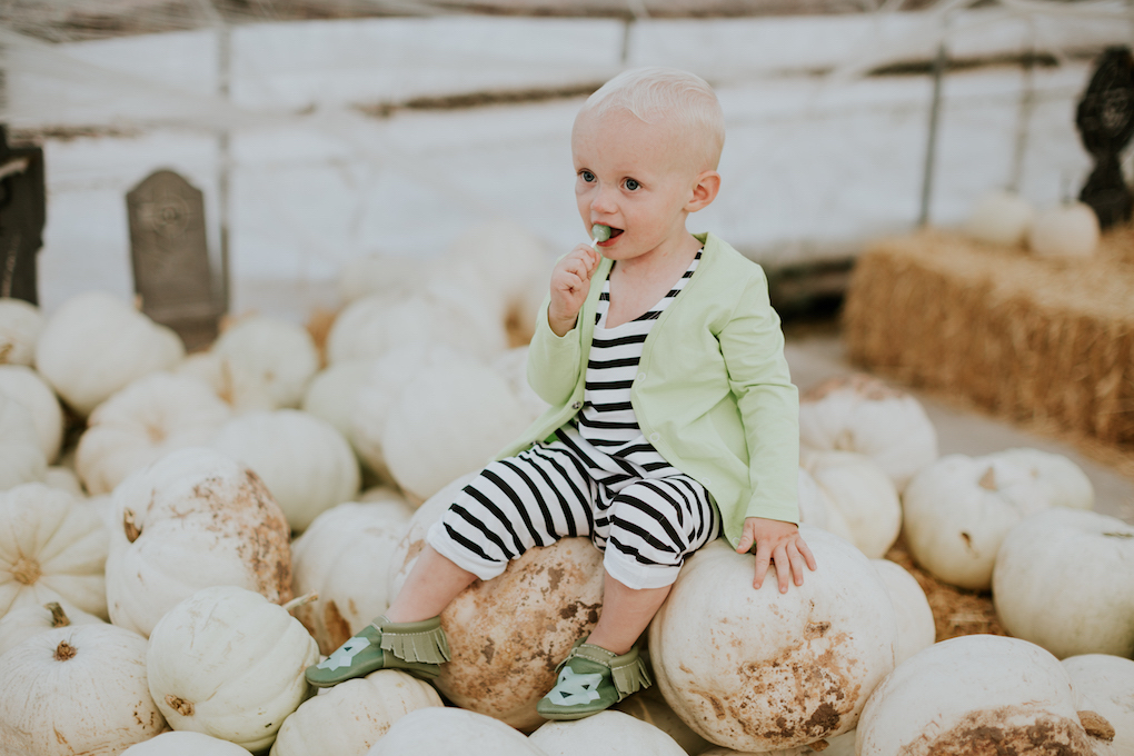 little boy sitting in pumpkin patch in black and white stripe romper and green cardigan june and january and freshly picked moccasins