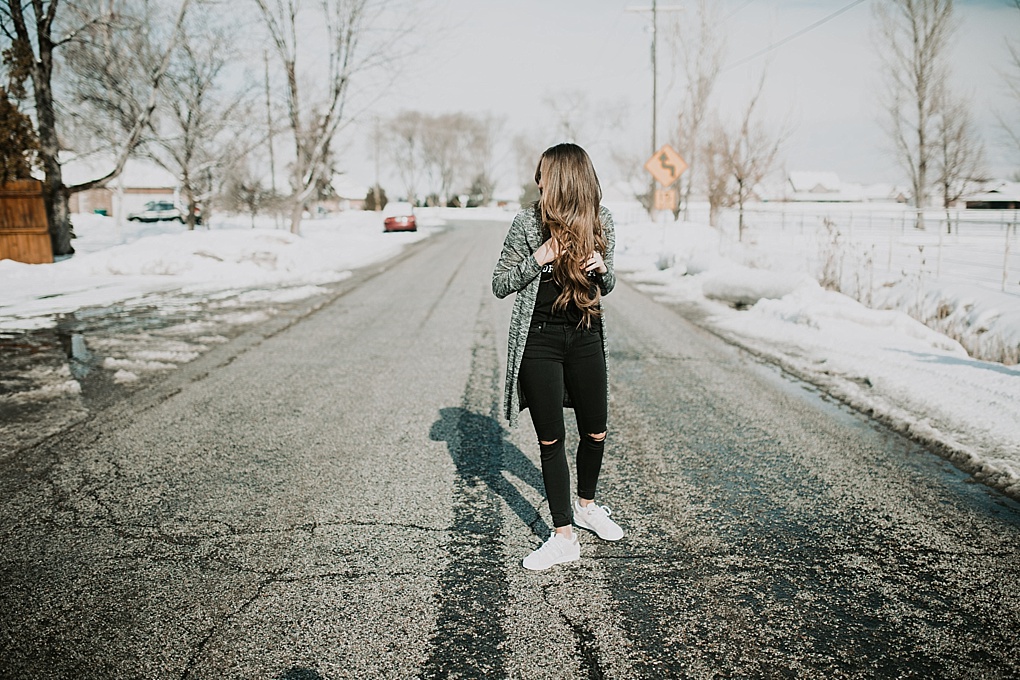 girl standing in road in black jeans with black tee shirt and long heathered grey black duster cardigan and blush pink adidas sneakers