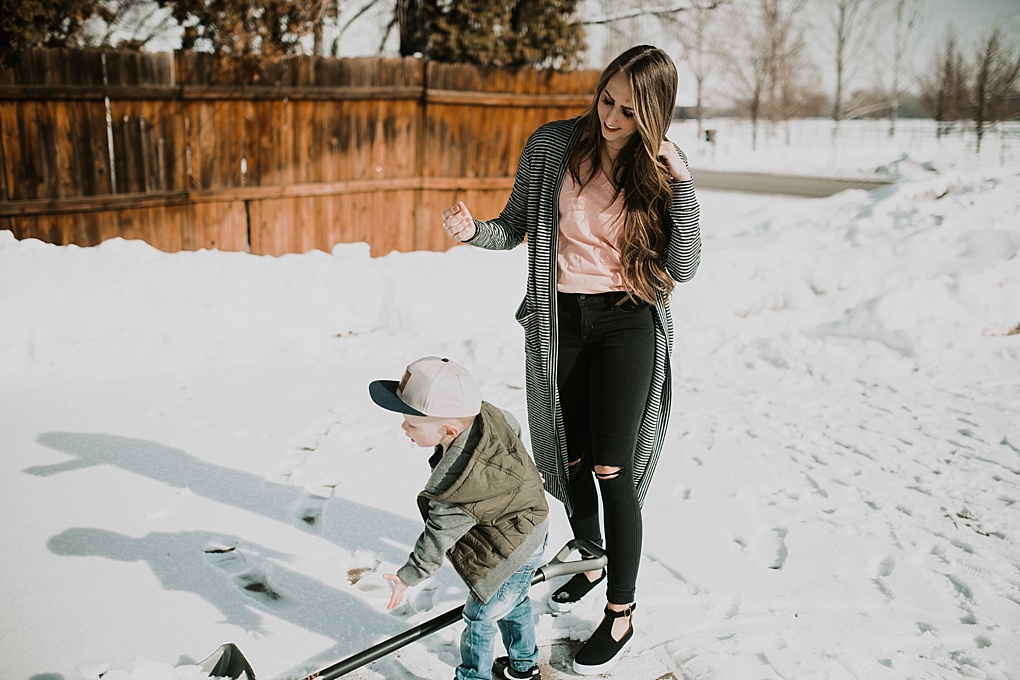 mom and little boy outside shoveling mom in long black and white stripe cardigan and little boy in army puffy jacket with jack and winn hat