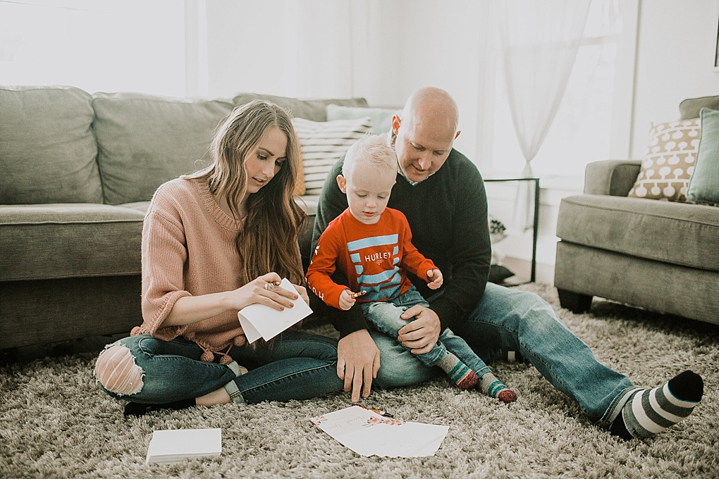 mom dad and little boy writing thank you cards from basic invite on rug in family room mom wearing pom pom sweater